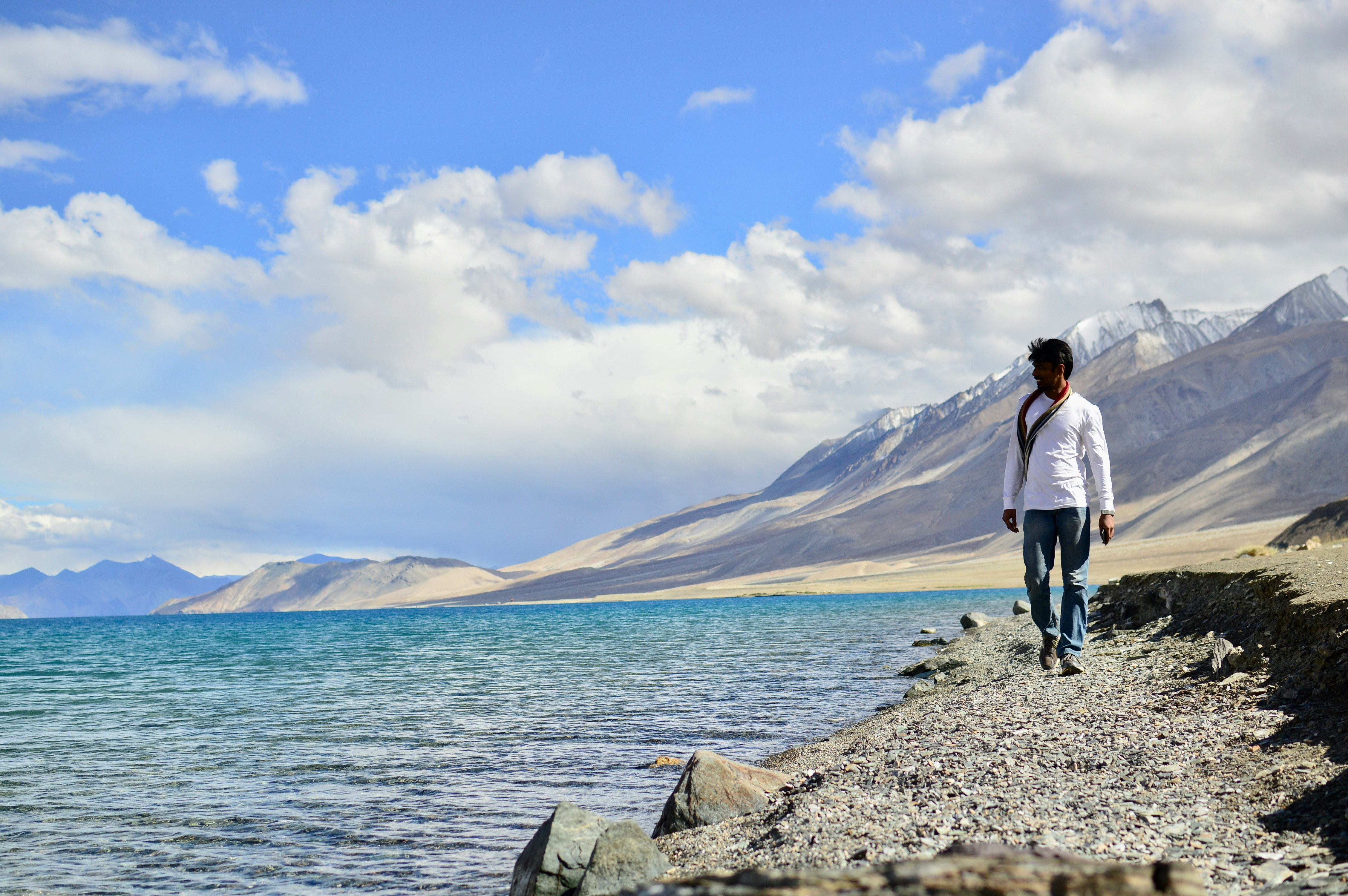 man in white shirt standing on gray rock near body of water during daytime